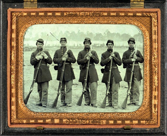 Five soldiers, four unidentified, in Union uniforms of the 6th Regiment Massachusetts Volunteer Militia outfitted with Enfield muskets in front of encampment