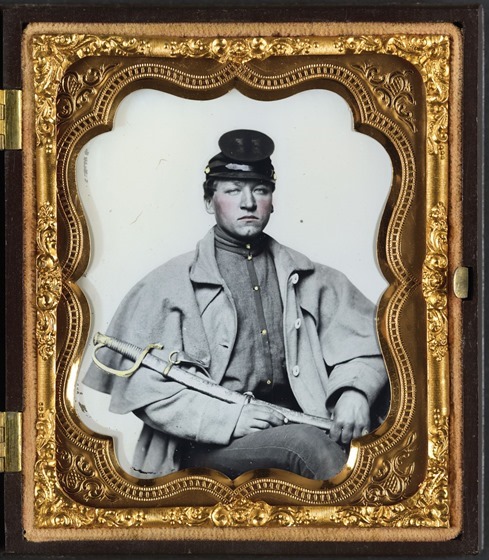 Unidentified soldier in Confederate artilleryman uniform and greatcoat with sword in case